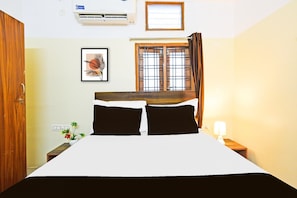 A hotel room with a bed, a window with curtains, a wall-mounted air conditioner, a framed picture, and a nightstand with a lamp. - Deluxe Hotel O Suncity Fort Inn (Hyderabad)