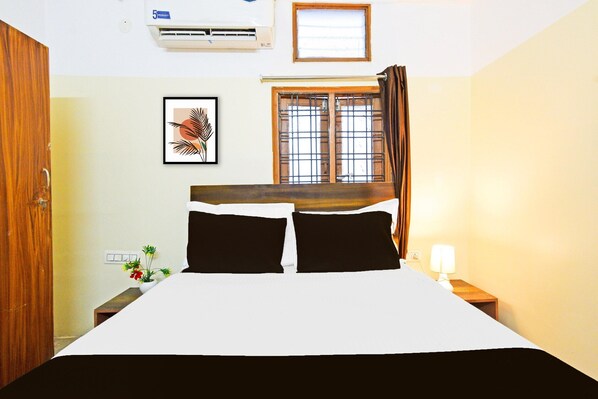 A hotel room with a bed, a window with curtains, a wall-mounted air conditioner, a framed picture, and a nightstand with a lamp. - Deluxe Hotel O Suncity Fort Inn (Hyderabad)