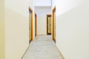 A hallway with marble flooring, wooden doors with intricate designs, and plain walls. - Deluxe Hotel O Suncity Fort Inn (Hyderabad)