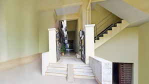 A corridor with a staircase leading to an upper level, a potted plant, and a metal gate. - Deluxe Hotel O Suncity Fort Inn (Hyderabad)