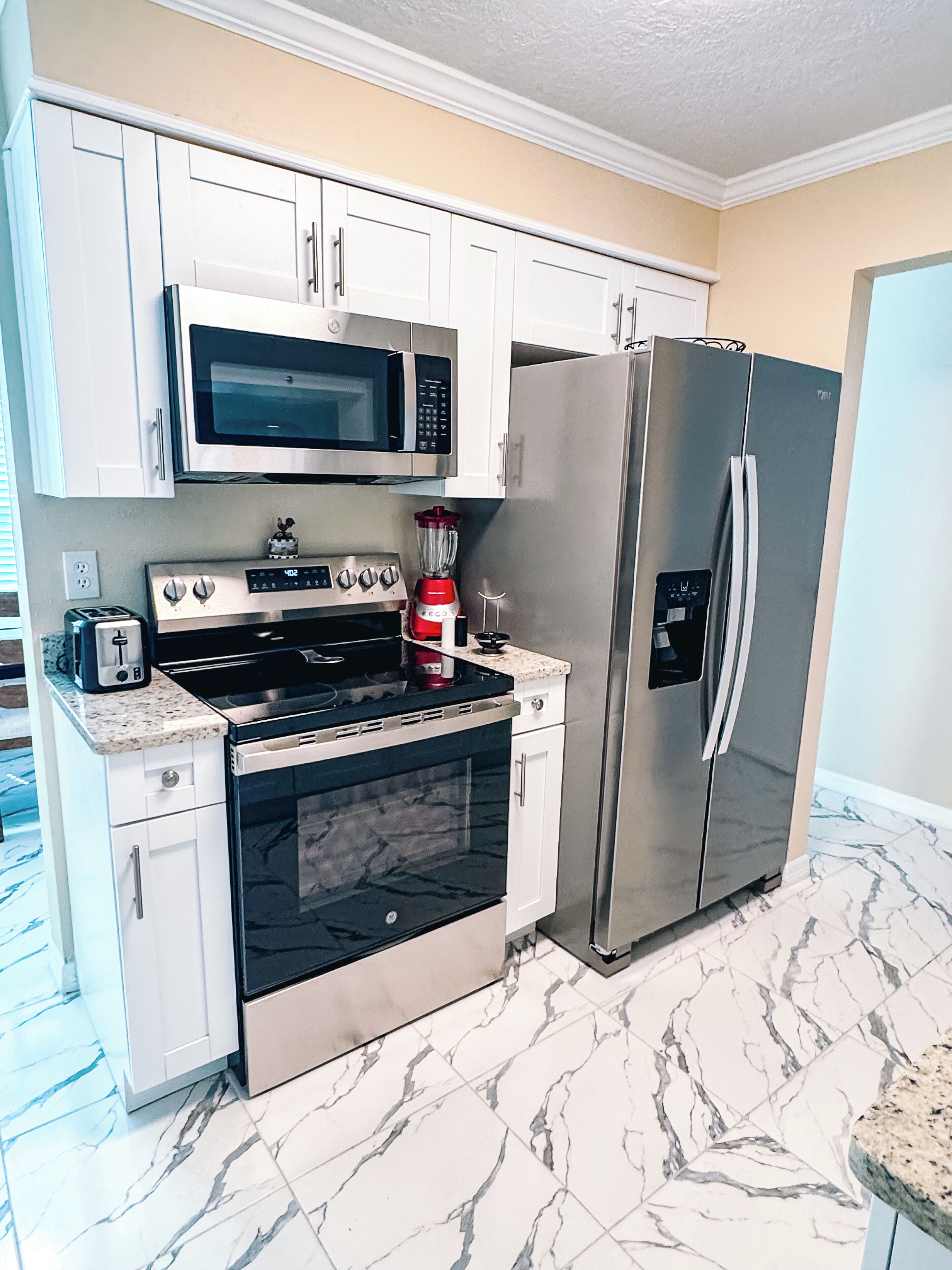A kitchen with white cabinets, a stainless steel refrigerator, a microwave, a stove, and a blender.