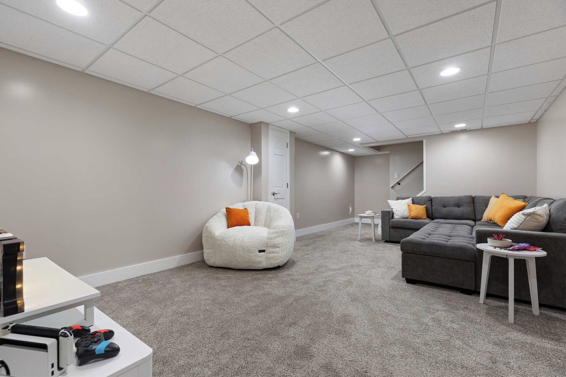 Une pièce comprenant un canapé d’angle gris, un fauteuil en forme de poire blanc, une petite table blanche et une porte blanche.