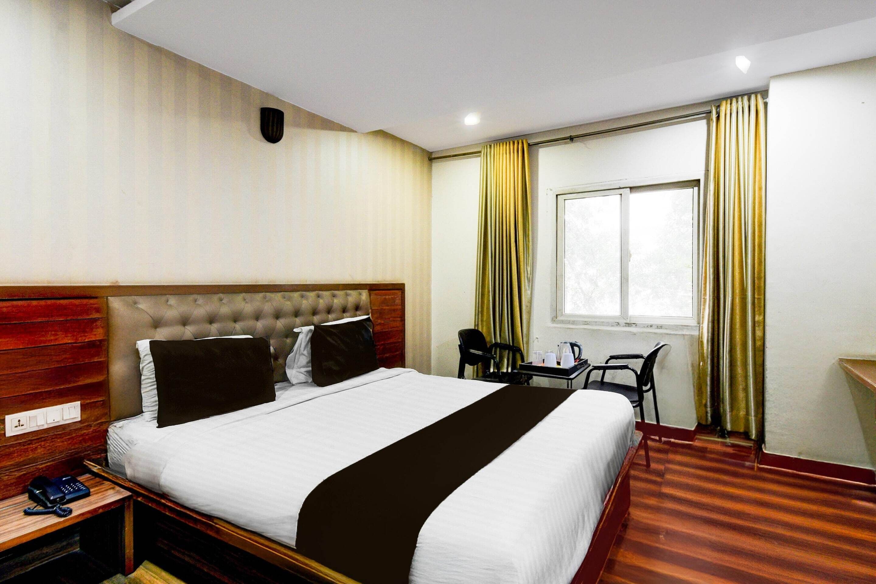 A hotel room with a bed, a desk, a chair, a window with curtains, and a wall-mounted telephone.