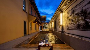 A narrow alleyway with a water feature, a table with a bottle and glasses, and a mural on the wall. - Aofeng Tangquan Secluded Villa (Dali)