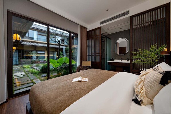Une chambre d’hôtel moderne avec un grand lit, une salle de bain avec un miroir et une vue sur un bâtiment traditionnel situé à l’extérieur.
