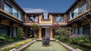 A courtyard with a central water feature, surrounded by a garden with various plants and a traditional building with balconies. - Aofeng Tangquan Secluded Villa (Dali)