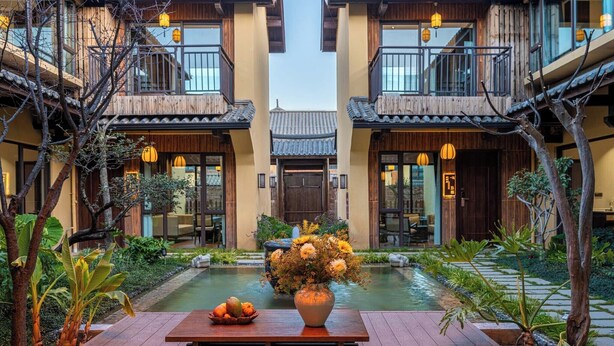 A courtyard with a wooden table, a vase of flowers, and a traditional building with a tiled roof. - Aofeng Tangquan Secluded Villa (Dali)