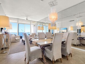 A spacious room with a large dining table, multiple chairs, and a view of the ocean through large windows. - Luxury Gulf Front Condo at Hidden Dunes! 18th Floor! (Miramar Beach)