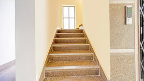 Una escalera con barandilla, una puerta al final y un panel de control de ascensor en la pared.