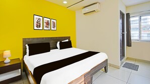 Un cuarto de hotel con cama, mesitas de noche, unidad de aire acondicionado, ventana con cortinas y una obra de arte en la pared.