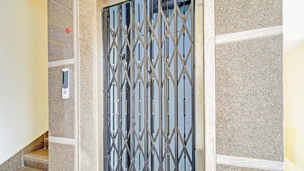 Una escalera con una reja metálica de seguridad, un portero automático en la pared y un muro de piedra texturizada.