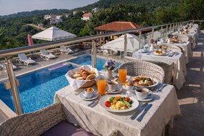 Ein Essbereich am Pool mit Tischen, gedeckt für das Frühstück, mit Blick auf einen Pool und eine malerische Hügellandschaft.