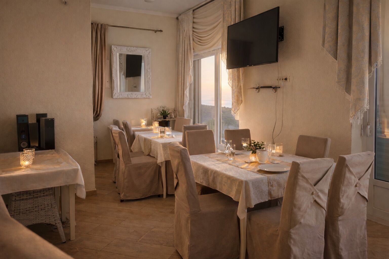 A dining area with tables set for four, a television mounted on the wall, and a window with curtains.