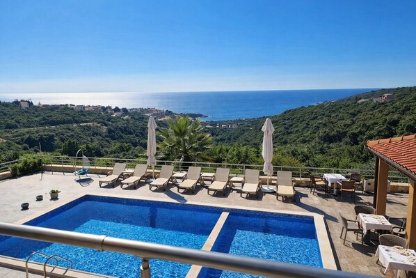 A pool with lounge chairs and umbrellas, overlooking a coastal landscape.