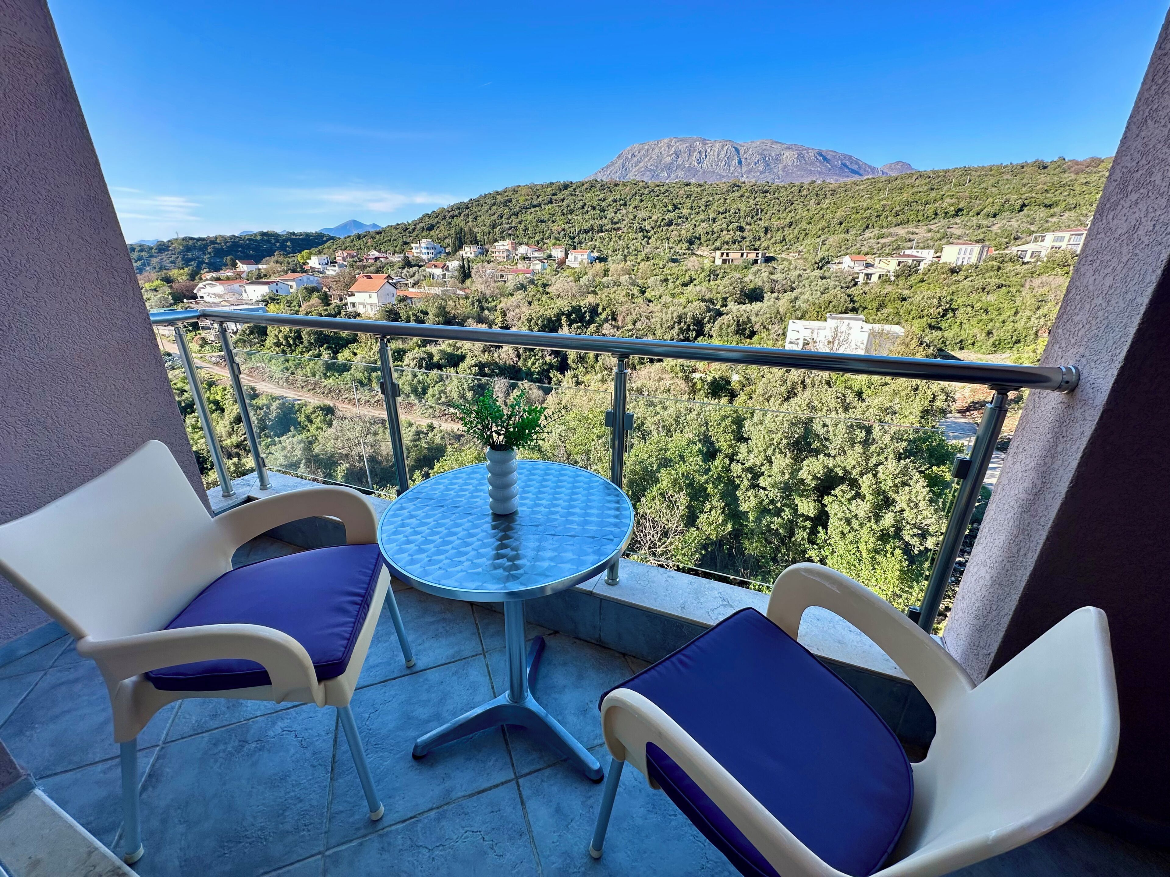 Ein Balkon mit zwei Stühlen und einem kleinen Tisch, der einen Blick auf einen Hügel mit Gebäuden und einem Berg bietet.