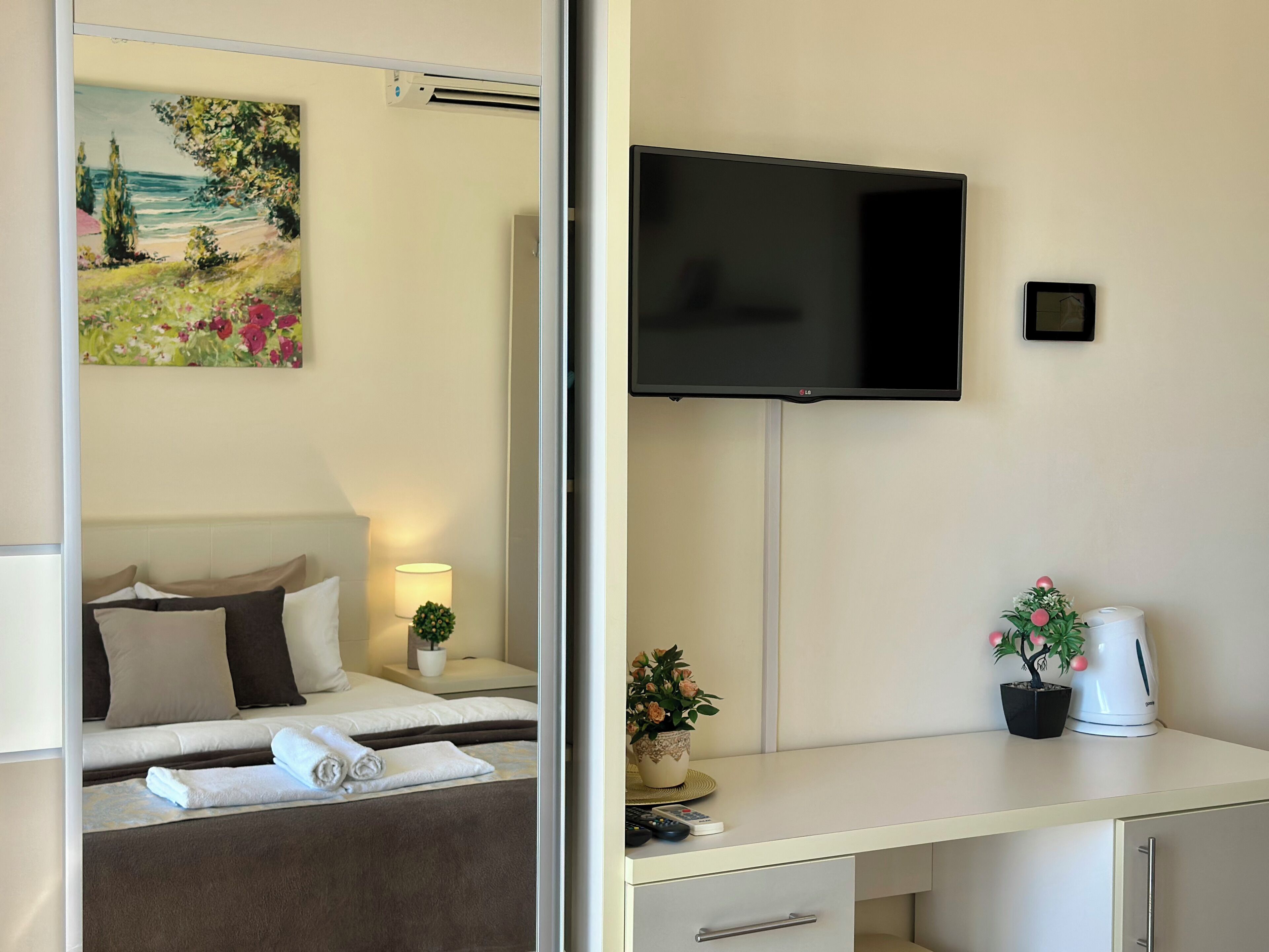 Una camera d'albergo con un letto, una scrivania con televisore, una piccola pianta in vaso e un bollitore.