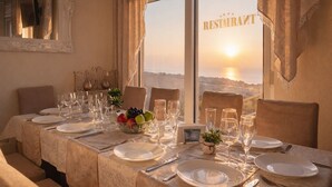 A dining table set for a meal with a view of the sunset through large windows. - Boutique-Apartments Edem (Utjeha)