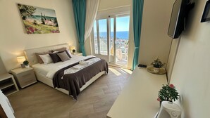 A hotel room with a bed, bedside table, lamp, and a view of the sea through a large window. - Boutique-Apartments Edem (Utjeha)