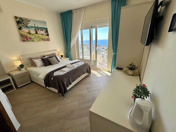 A hotel room with a bed, bedside table, lamp, and a view of the sea through a large window.