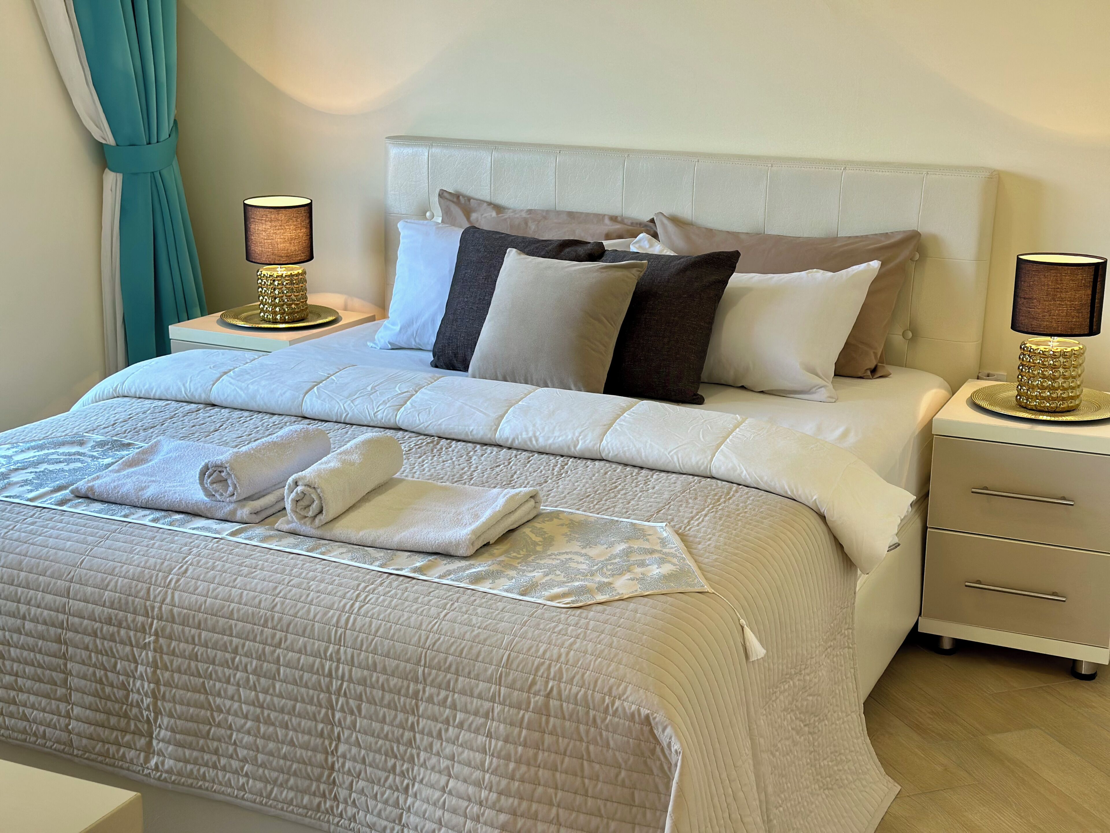 A neatly made bed with a quilted cover, two bedside lamps, and a bedside table with a decorative item.