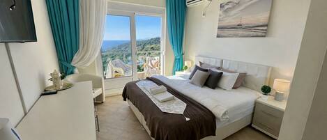 A hotel room with a bed, a TV, a window with curtains, a painting, and an air conditioning unit.