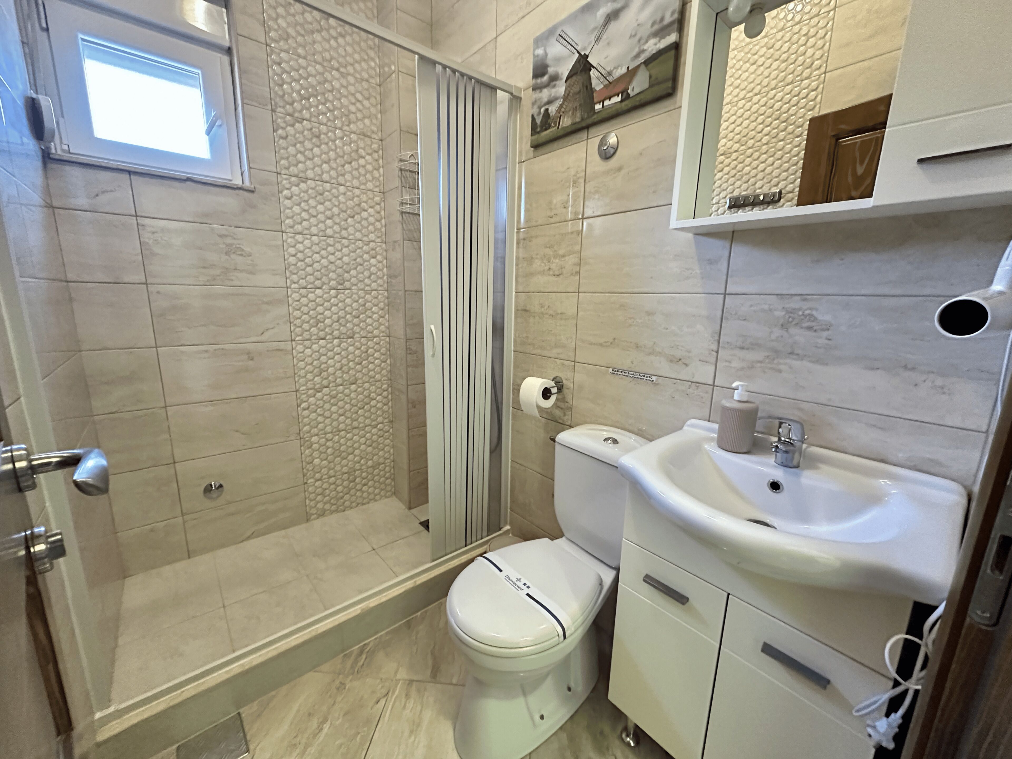 A bathroom with a shower, toilet, sink, and a window.