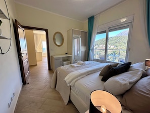 Ein Schlafzimmer mit einem Bett, einem Nachttisch und einem Fenster mit Blick auf eine Berglandschaft.
