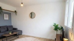 Ein Wohnzimmer mit grauem Sofa, einem runden Teppich, einem Couchtisch, einem Beistelltisch mit Lampe und einem Spiegel an der Wand.