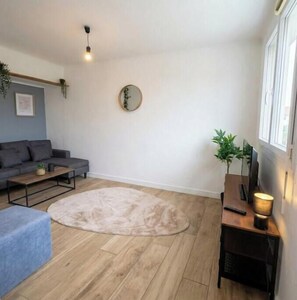 Ein Wohnzimmer mit grauem Sofa, einem runden Teppich, einem Couchtisch, einem Beistelltisch mit Lampe und einem Spiegel an der Wand.