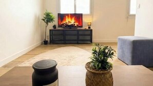 Ein Wohnzimmer mit Kamin, Fernseher, einer Pflanze und einer Kerze auf einem Tisch.
