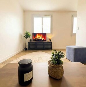 Ein Wohnzimmer mit Kamin, Fernseher, einer Pflanze und einer Kerze auf einem Tisch.