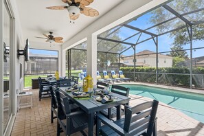 Un patio techado al aire libre con mesas y sillas, una piscina y vistas del barrio.