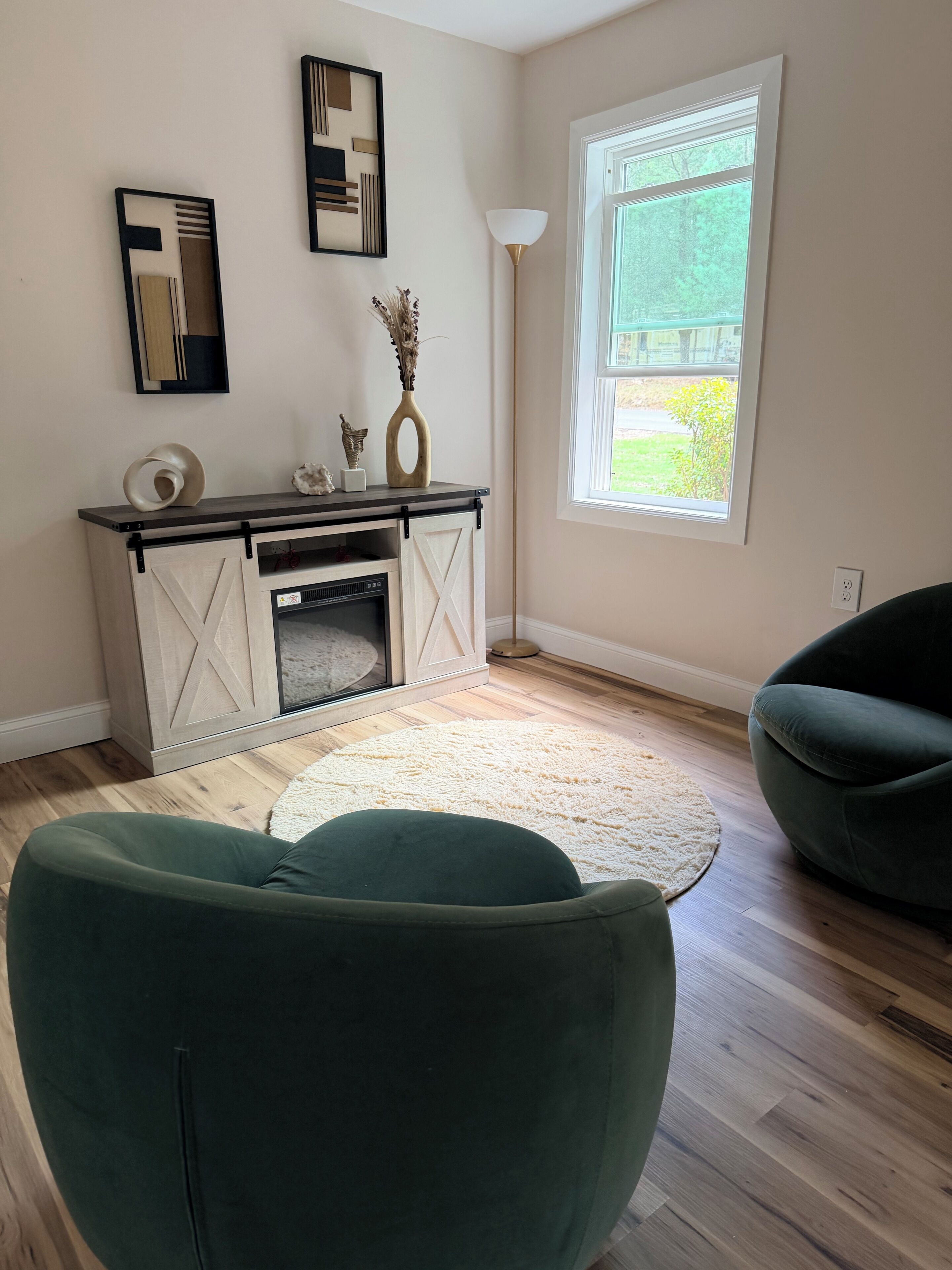 A living room with a fireplace, a large window, and two green armchairs.