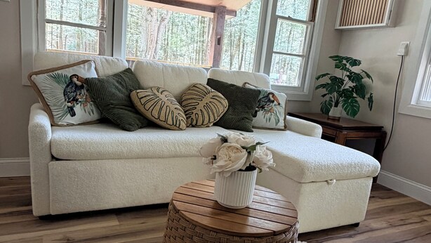 A living room with a sofa, pillows, a round wooden side table, and a white fluffy rug.