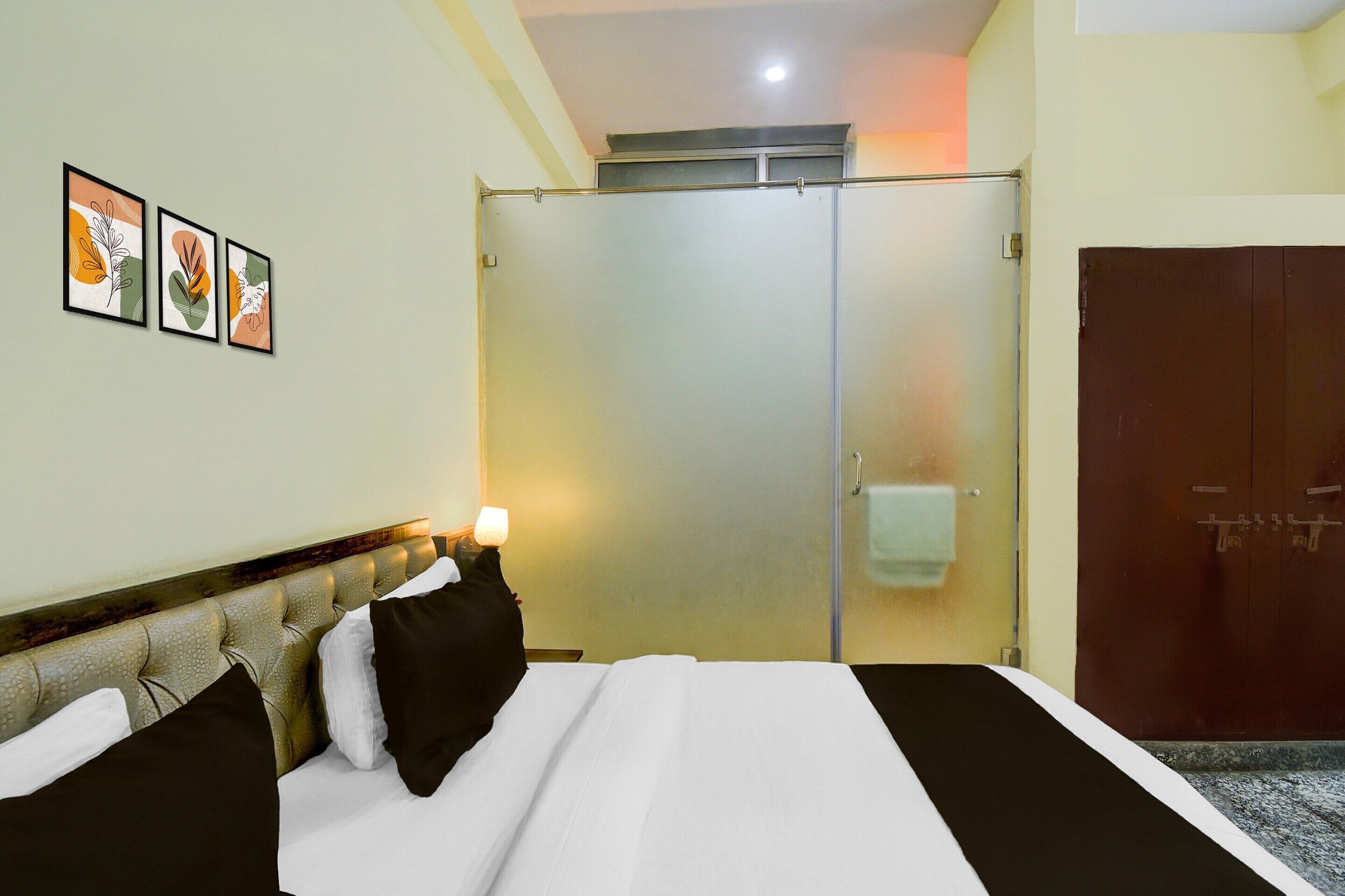 A hotel room with a bed, a wardrobe, a glass door, and three framed pictures on the wall.