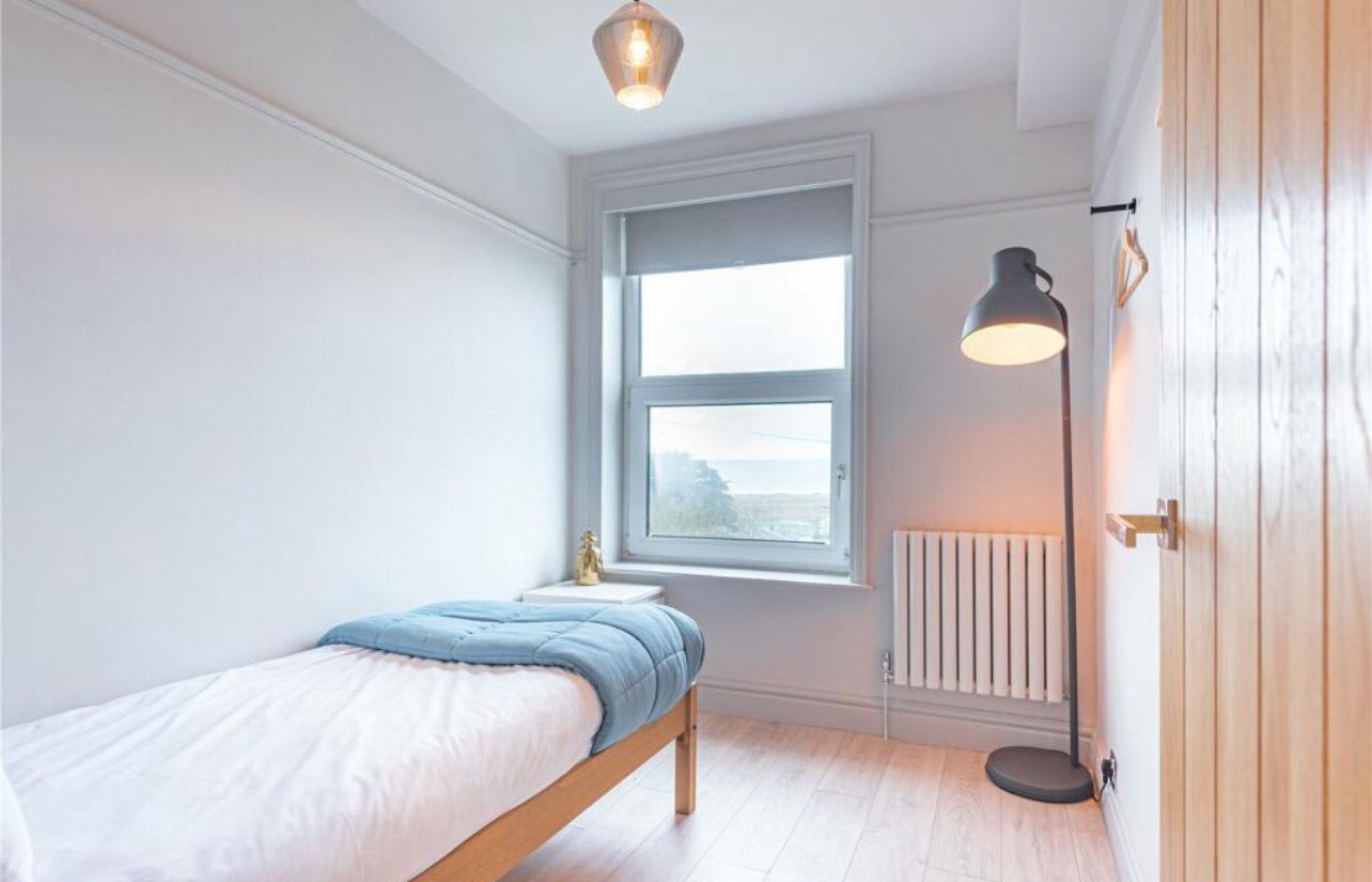A bedroom with a bed, a window, a radiator, and a floor lamp.