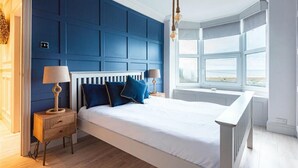 Ein Schlafzimmer mit einem großen Bett, einem Nachttisch, einer Lampe, einem Fenster mit Aussicht und einer Deckenleuchte.