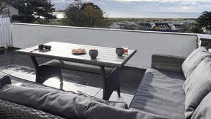 Eine Dachterrasse mit Tisch, Stühlen und Blick auf den Strand.