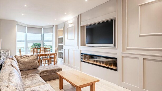 Ein Wohnzimmer mit einer Couch, einem Holztisch, einem Kamin und einem an der Wand befestigten Fernseher.