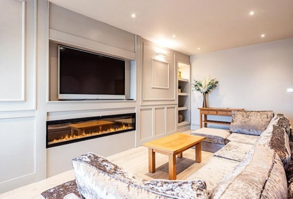 A living room with a fireplace, a large flat-screen TV, a sofa, and a coffee table.