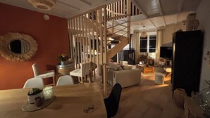 A modern living room with a wooden partition, a dining area with a table and chairs, and a staircase leading to an upper level.