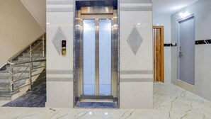 Een lift in een hotellobby met een marmeren vloer en een trap aan de linkerkant.