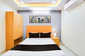 Habitación de hotel con cama, armario, mesita de noche, lámpara y tres obras de arte colgadas en la pared.