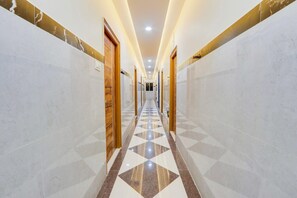 Un pasillo de hotel con paredes de mármol, piso de diseño geométrico y puertas de madera.