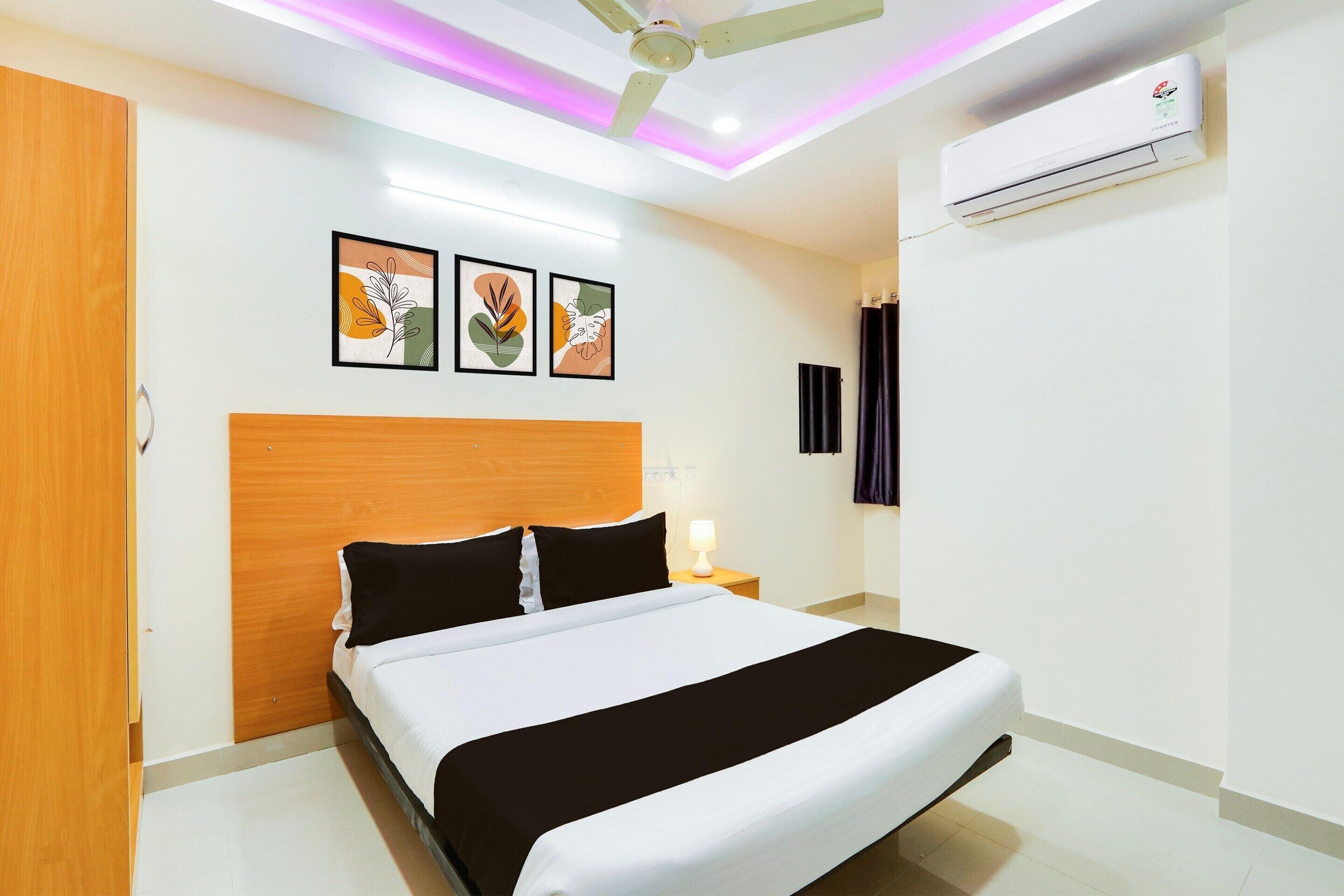 A hotel room with a bed, a ceiling fan, an air conditioner, and wall-mounted artwork.