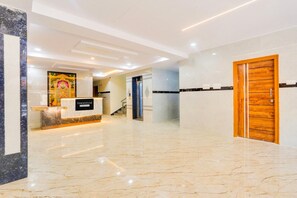 Zona de recepción de un hotel con suelo de mármol, mostrador de recepción, una escalera y una puerta de madera.