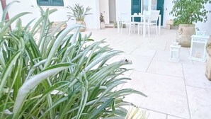 Un patio con plantas en macetas, muebles de exterior blancos y piso de baldosas.