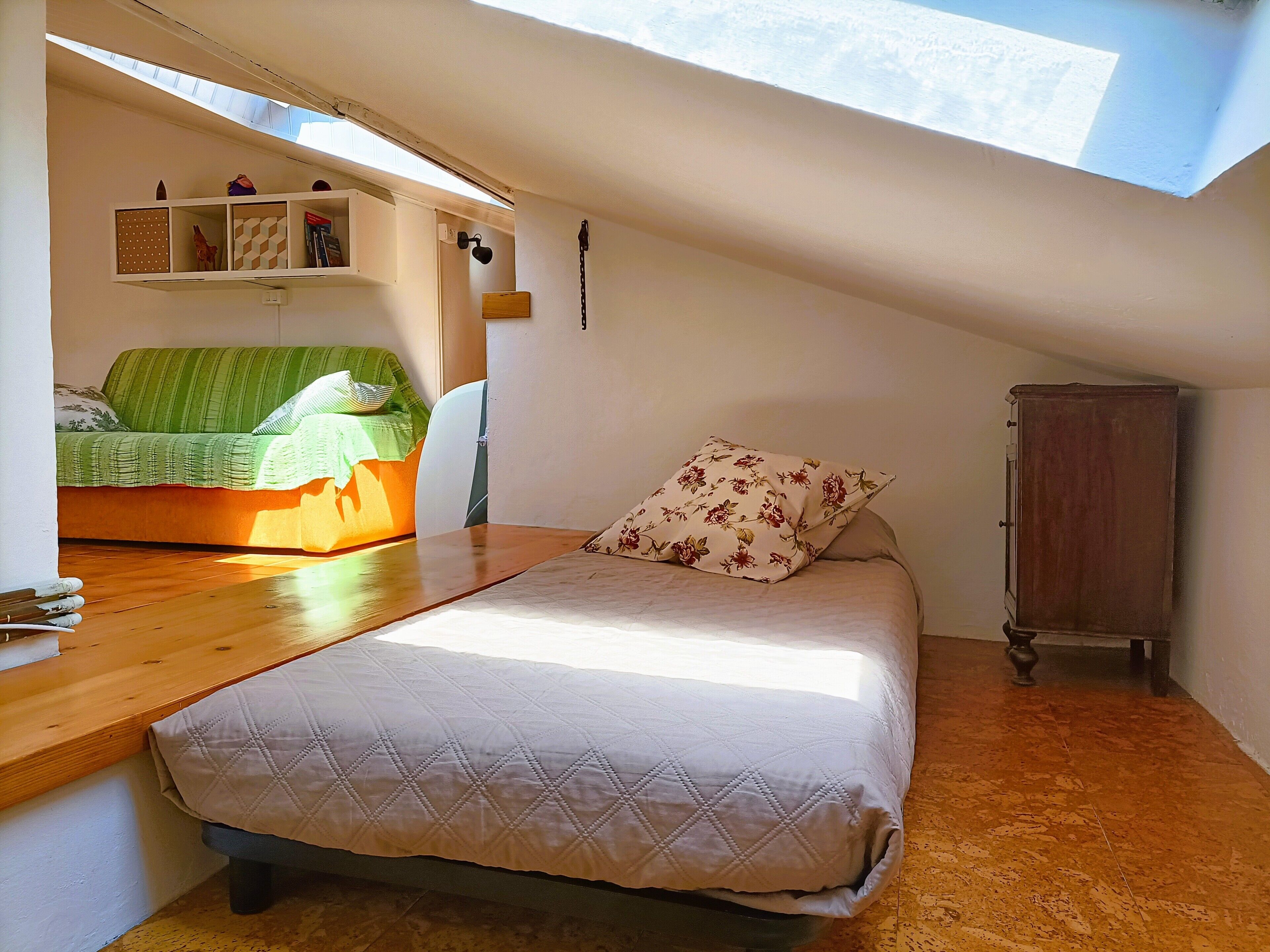 A bedroom with a bed, a desk, a chair, a wardrobe, and a skylight.
