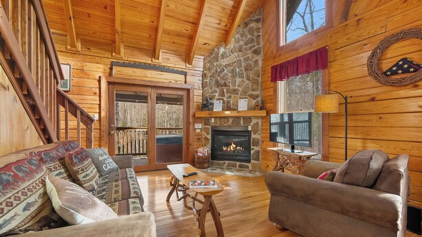 A log cabin interior with a stone fireplace, wooden furniture, and a staircase. - Rocky Top Sports World - 7 mins, Gatlinburg getaway w/Hot tub & Outdoor games (Gatlinburg)