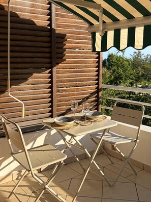 Een balkon met een tafel voor twee personen, twee stoelen en een gestreept zonnescherm.
